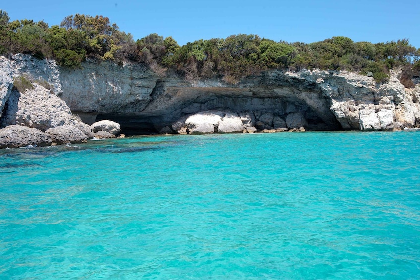 A coastal scene with clear turquoise waters, a rocky cliff, and dense green vegetation. 2
