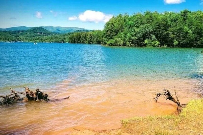 A river with clear water, a sandy shore, and a forested hill in the background. 5
