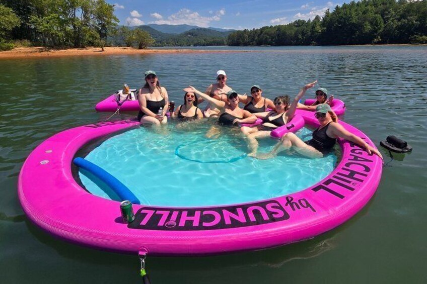 A group of people in a pink inflatable pool on a lake surrounded by trees and hills. 3