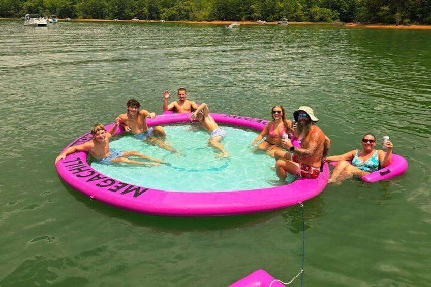 A group of people in a pink inflatable pool on a lake surrounded by greenery. 4
