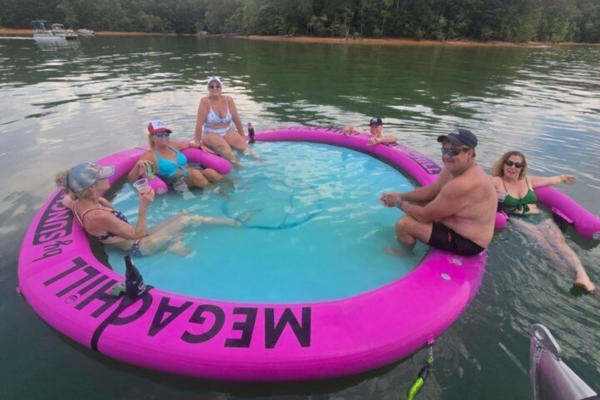 A group of people in a pink inflatable pool on a lake surrounded by trees. 5