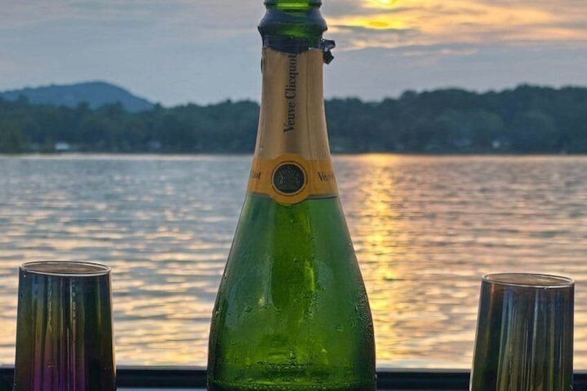 A green bottle with a label, two glasses, and a scenic view of a lake with mountains in the background. 3