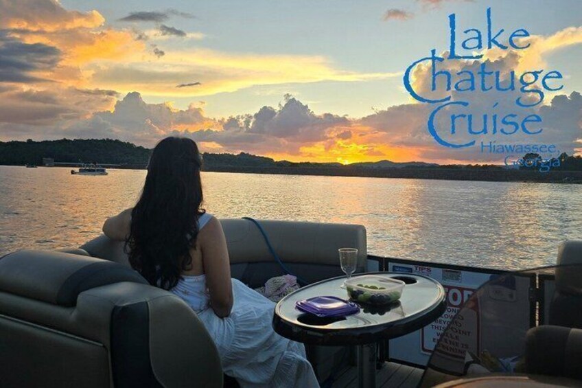 A woman sitting by a lakeside at sunset, with a boat in the background. 2
