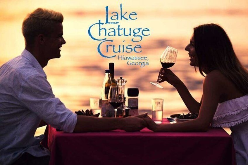 A couple dining at sunset by a lake with a table set for two, a bottle of wine, and glasses. 1
