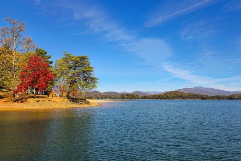 A calm lake with autumn trees, a clear sky, and distant mountains. 1