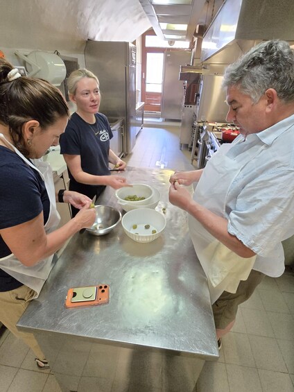 A group of people preparing food in a kitchen with stainless steel countertops and various cooking utensils. 3