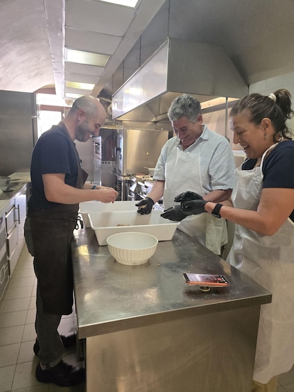 A kitchen with three people preparing food, a white bowl on the counter, and a smartphone. 2