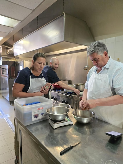 A kitchen with stainless steel countertops, a person cooking on a stove, and another person using a phone. 5