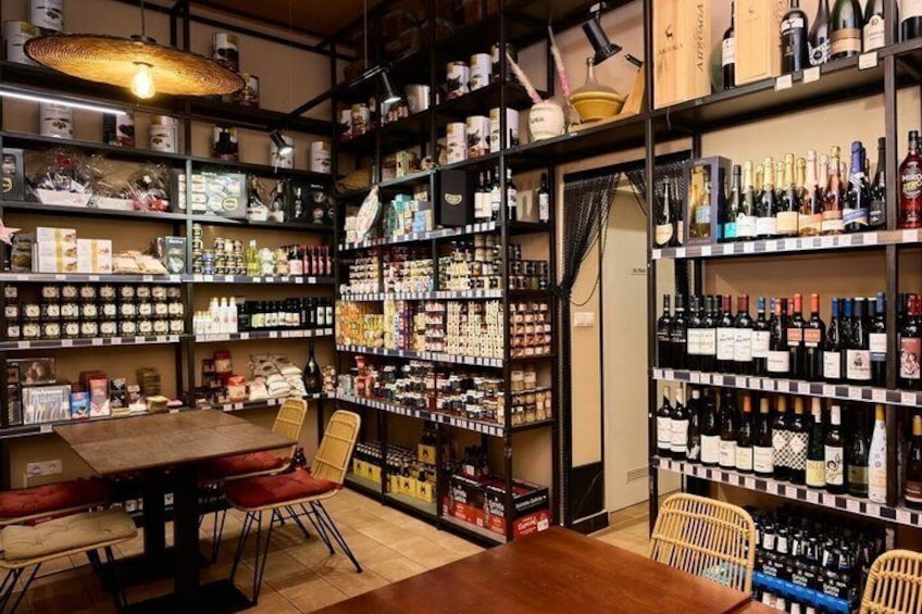 A store with shelves stocked with various products, a wooden table, and chairs. 3