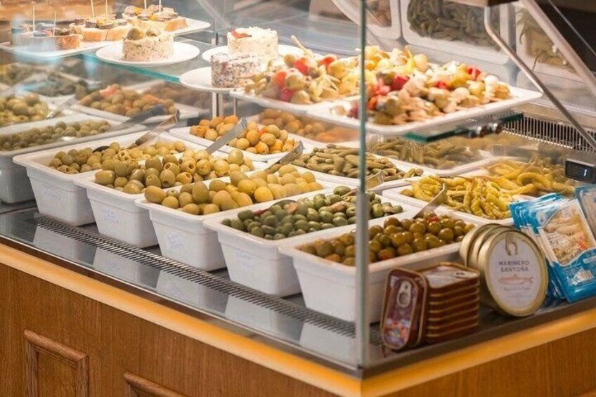 A deli counter with various food items, including trays of olives, pickles, and packaged meats. 5