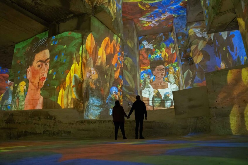 Two people observing a large, colorful mural with abstract and realistic elements. 2