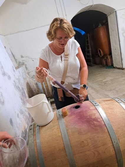 A person pouring liquid from a bottle into a wooden barrel. 2