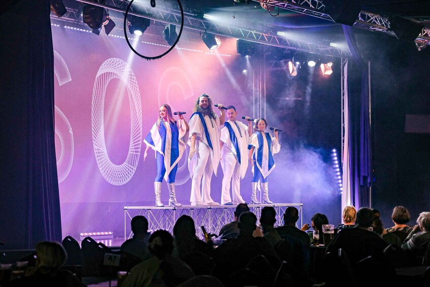A group of performers on stage with a large '50' backdrop, wearing matching costumes. 4