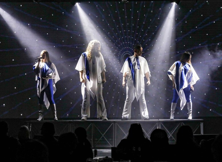 A stage with four performers in dynamic poses, illuminated by spotlights against a dark background with a starry pattern. 1