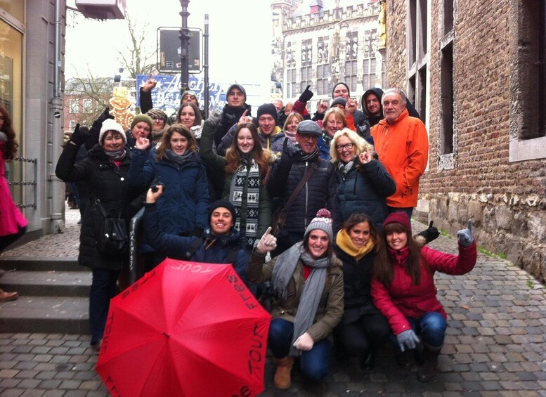 A group of people posing for a photo in a historic European street with cobblestone pavement and brick buildings. 1