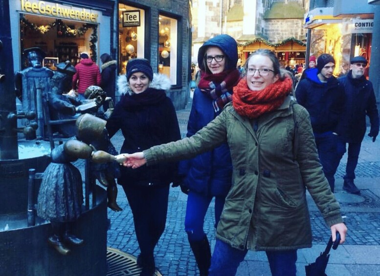 A group of people walking on a cobblestone street with shops and a statue in the background. 2