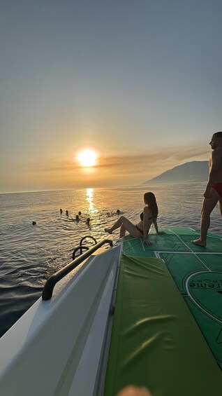 Ein Sonnenuntergang über einem Gewässer mit Menschen in einem Boot und im Wasser. 1