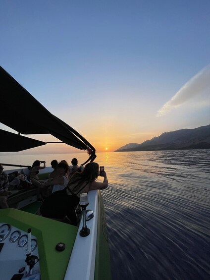 Ein Sonnenuntergang über ruhigem Wasser, mit einem Boot und Personen darin. 2