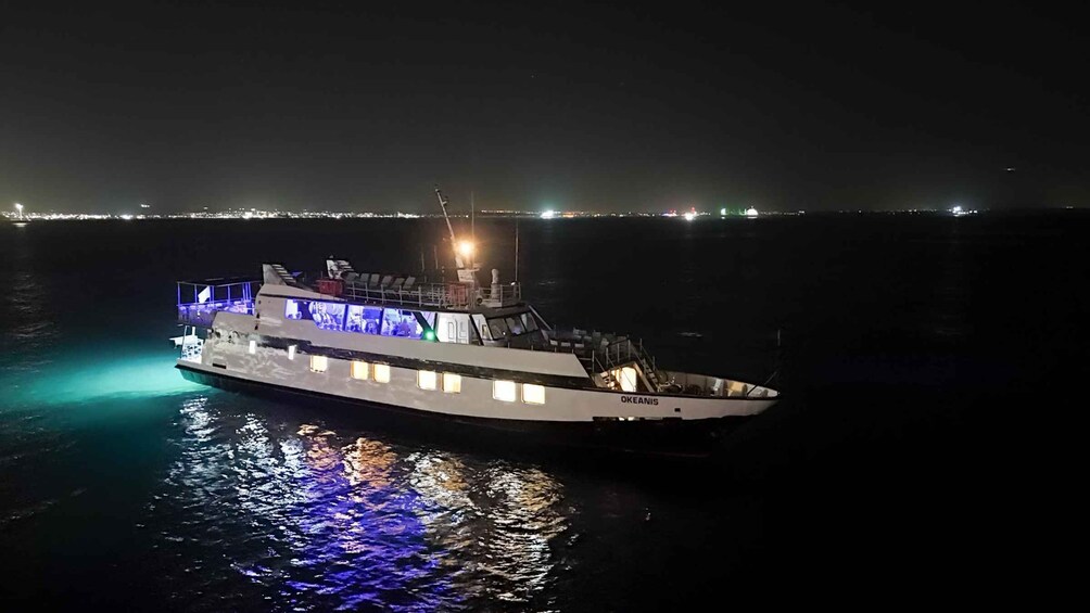 A boat named 'Okeanis' with illuminated windows and a crane on a calm water body at night. 1