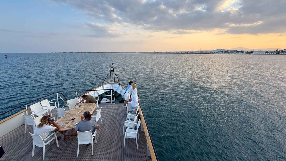 A boat with people on deck, a sunset in the background, and calm water. 4