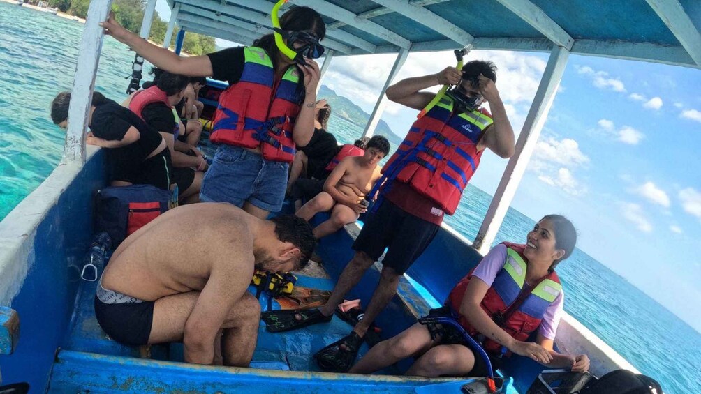 Eine Gruppe von Menschen in Schwimmwesten auf einem Boot, einige mit Schnorchelausrüstung, auf dem Wasser unter blauem Himmel. 4