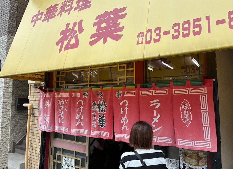 A storefront with a yellow awning and red banners with Japanese characters. 5