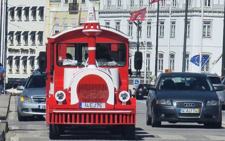A red and white vintage tram on a city street with modern cars and buildings in the background. 2