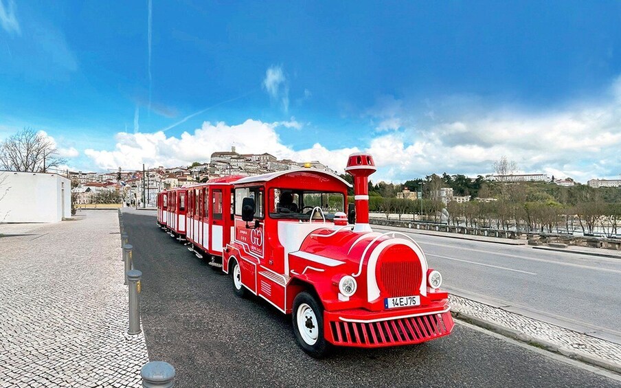 A red and white train on a paved road with a clear sky and distant buildings. 5