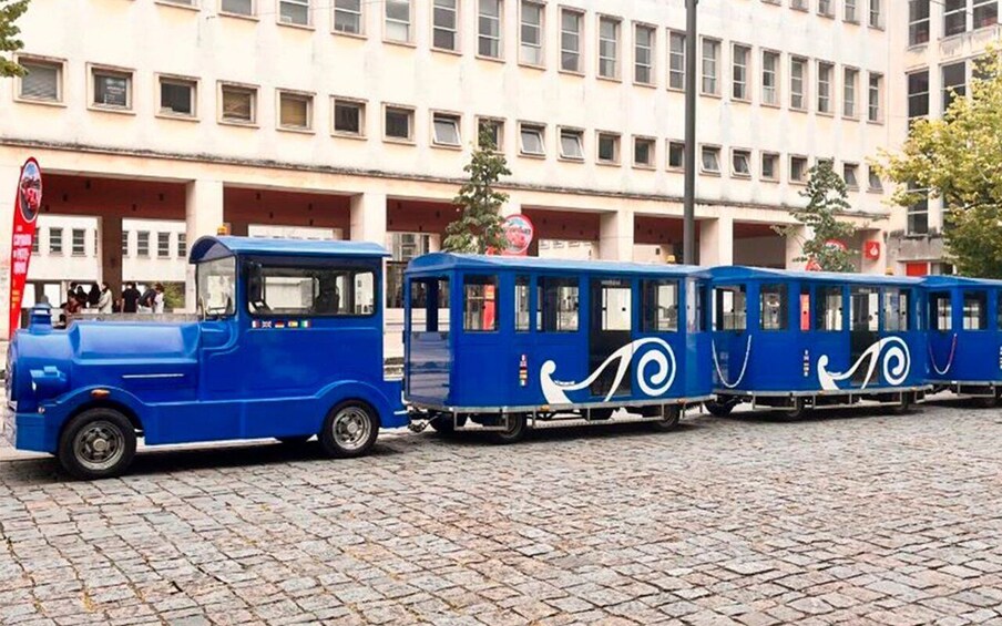 A blue tram with white wave designs parked on a cobblestone street. 4