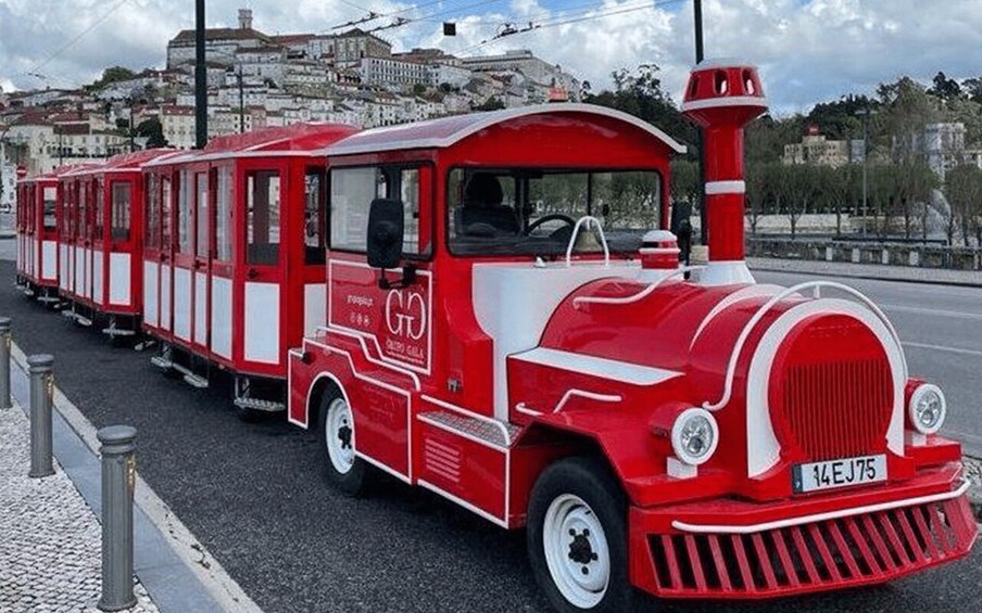 A red and white vintage tram with the license plate 14 EJ 75, parked on a street with a historical building in the background. 1