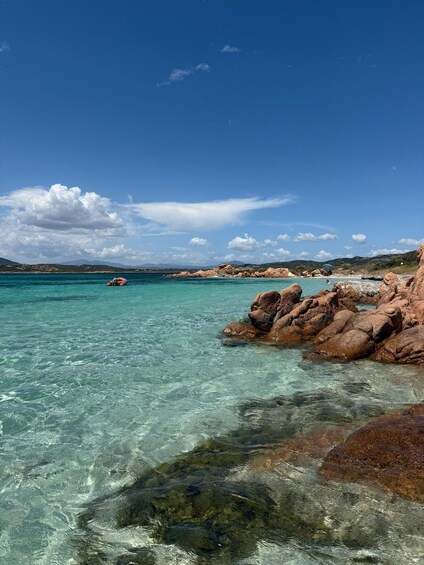 A clear turquoise sea, rocky shoreline, and distant mountains under a blue sky. 2