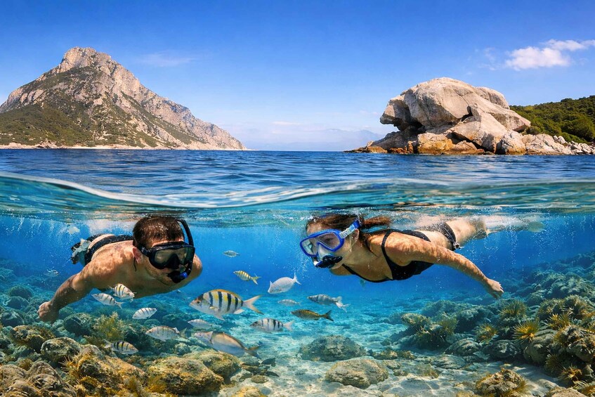 Two snorkelers swimming underwater with fish and coral reefs, with a mountainous landscape in the background. 1