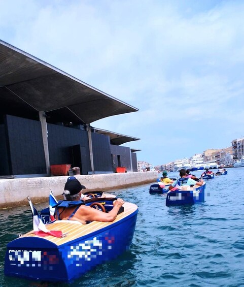 People in pixelated blue boats on a waterway with buildings in the background. 2