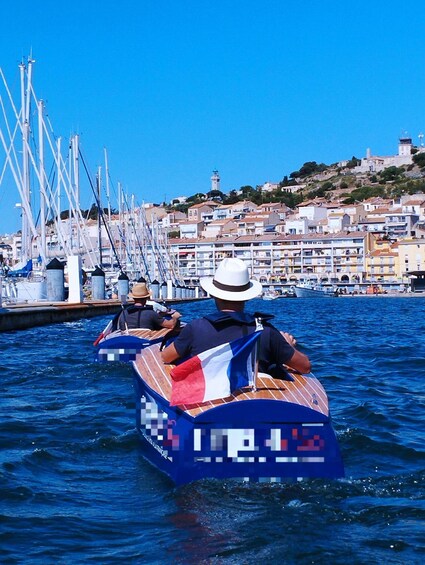 A row of canoes on a calm body of water, with a town and lighthouse in the background. 3