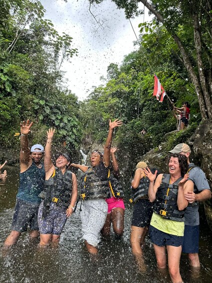 A group of people in a forested area with a waterfall, wearing life jackets and enjoying the water. 1