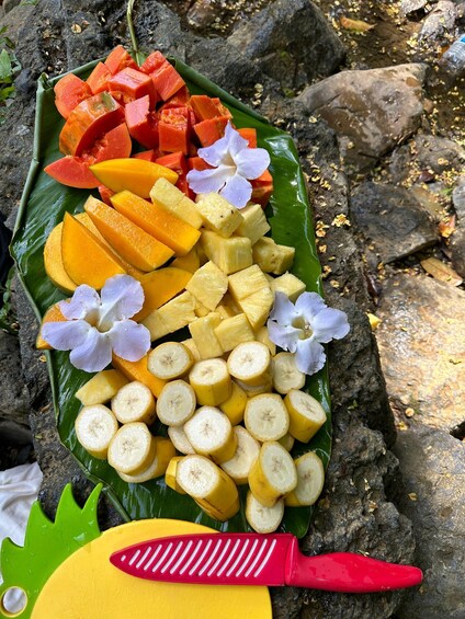 A banana leaf platter with sliced fruits and flowers. 2