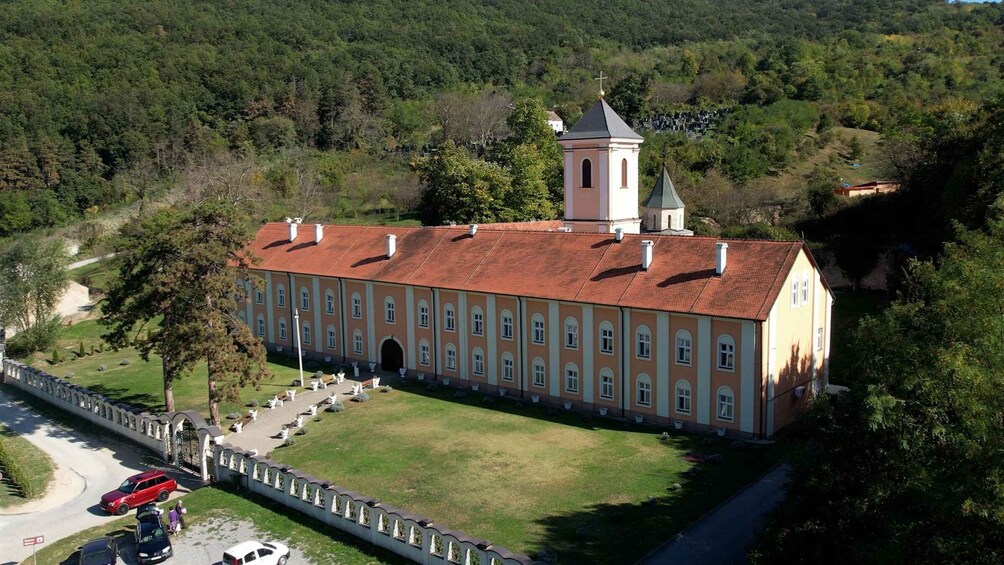 A large, historic building with a red-tiled roof, surrounded by a well-maintained lawn and a stone wall. 3
