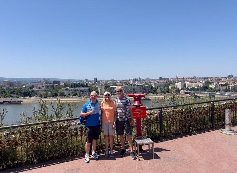 Three people standing on a bridge with a cityscape in the background. 4