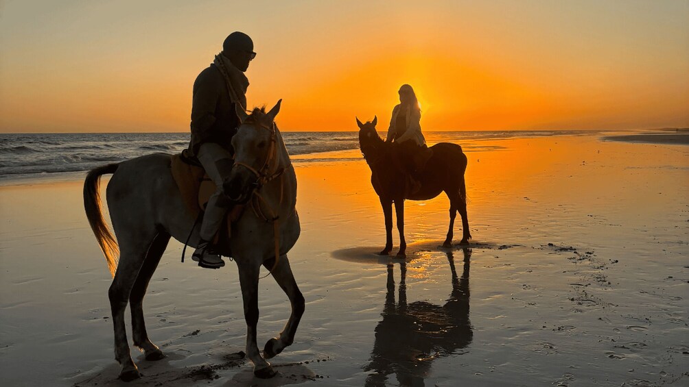 Two people riding horses on a beach at sunset. 3