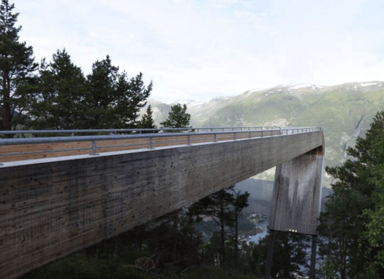 A concrete bridge with a metal railing, surrounded by trees and a mountainous landscape. 3