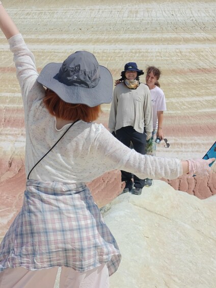 A person in a plaid skirt and a hat, holding a blue object, standing on a textured surface with a person in the background. 2