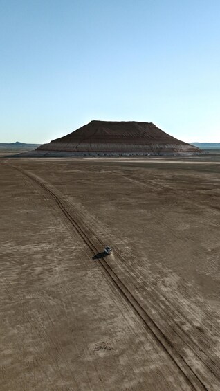 A barren landscape with a large mound in the distance and a vehicle on the ground. 1