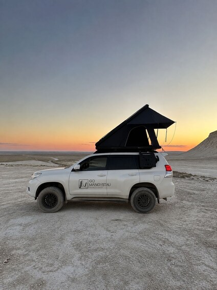 A white SUV with a black roof tent parked on a sandy beach at sunset. 5