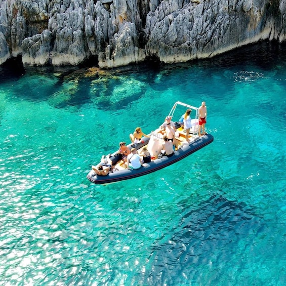A group of people on a boat in clear turquoise water with rocky cliffs in the background. 2