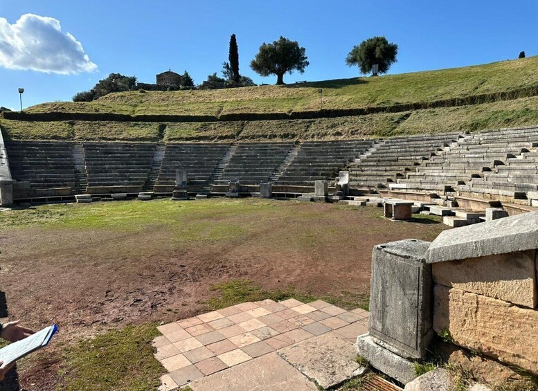 An ancient amphitheater with stone seating and a grassy hill in the background. 5