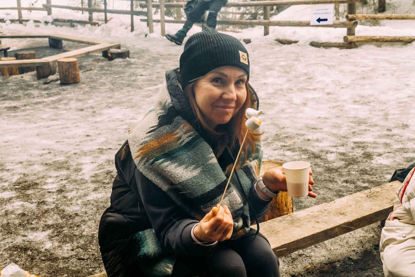A person sitting on a bench in a snowy outdoor setting, holding a cup and wearing a beanie. 4