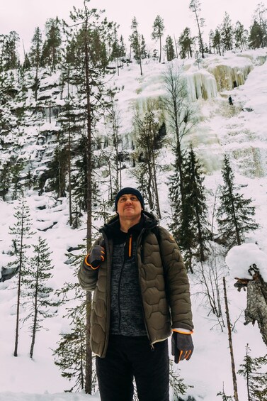 A person standing in a snowy forest with trees and a waterfall in the background. 3