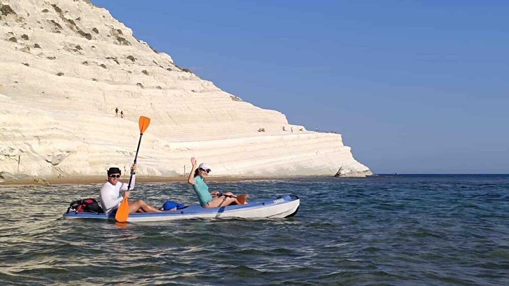 Two people kayaking on calm waters with a white cliff in the background. 1