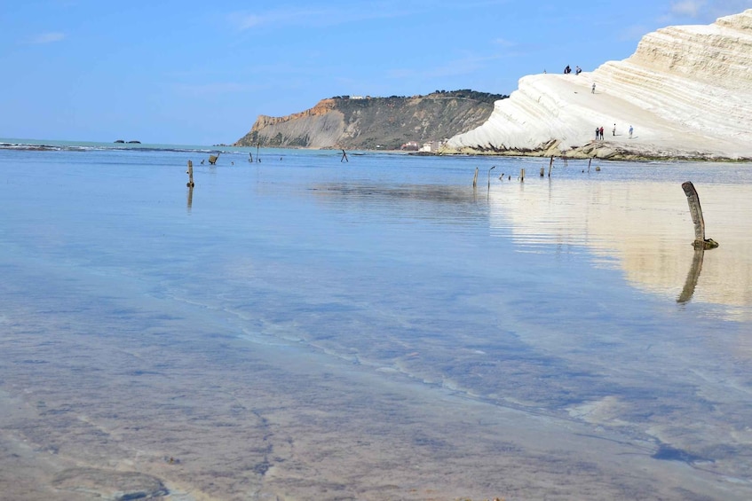 A beach with clear water, white cliffs, and a few people walking. 4