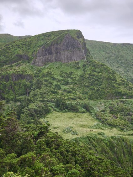 A lush green mountain with a prominent rocky peak and dense forest. 2